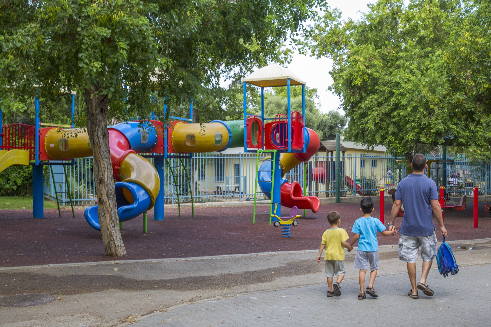 אב ושני ילדיו בגן שעשועים צמוד לפרויקט, ברקע מגלשות.